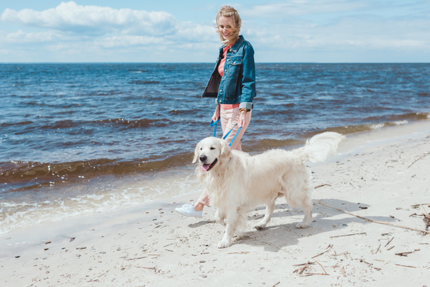 beautiful woman walking with golden retriever dog on sea shore - Фото, зображення