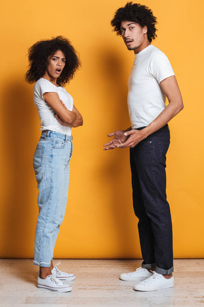 Full length portrait of a confused afro american couple having an argument isolated over yellow background - Foto, Bild