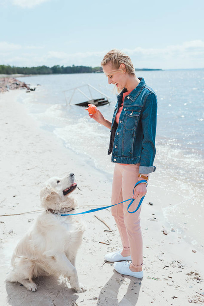 woman playing ball with golden retriever dog on sea shore - Fotografie, Obrázek