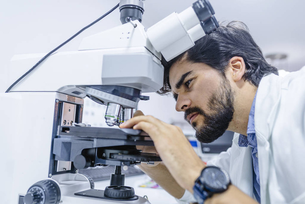 Young Student Researcher Man Work with Lab Microscope.  Handsome man examining glass slide samples while working at his lab microscope. Close-up of a male scientific researcher - Φωτογραφία, εικόνα