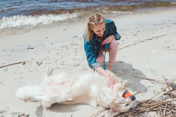 smiling woman playing ball with golden retriever dog on shore - Zdjęcie, obraz