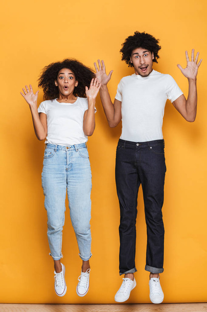 Full length portrait of a cheerful young afro american couple jumping together isolated over yellow background - Fotoğraf, Görsel