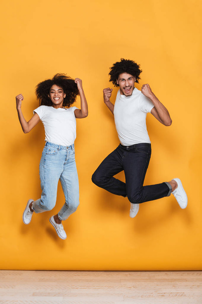 Full length portrait of a smiling young afro american couple jumping together isolated over yellow background - Photo, Image