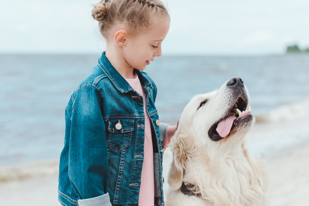  adorable child with friendly golden retriever dog on sea shore - Foto, afbeelding