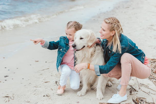 семья с золотой собакой-ретривером на берегу моря, дочь куда-то указывает
 - Фото, изображение