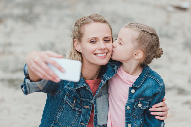 suloinen tytär suudella äitiä, kun hän ottaa selfie älypuhelimeen
  - Valokuva, kuva