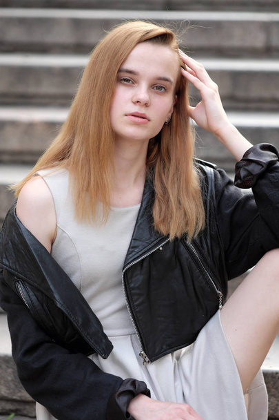 young and sexy redheaded girl posing outdoors in leather jacket and gown - 写真・画像