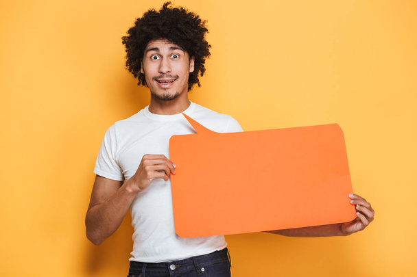 Portrait of a happy young african man holding empty speech bubble isolated over yellow background - Foto, Imagen