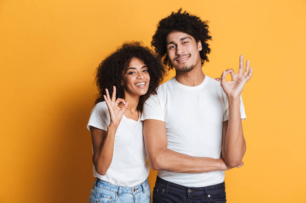Portrait of a happy afro american couple showing ok gesture isolated over yellow background - Foto, Bild