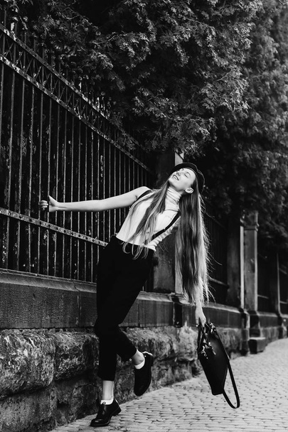 een dromerige meisje houdt haar hand achter het hek door het opheffen van een been op een zwart-wit foto - Foto, afbeelding