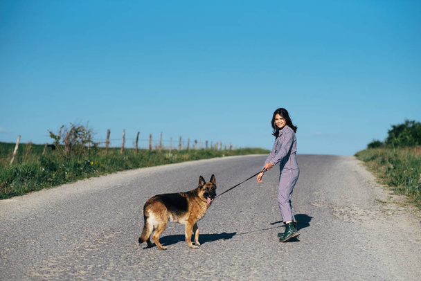 A pretty girl leads a dog next to her on the road. - Foto, Bild