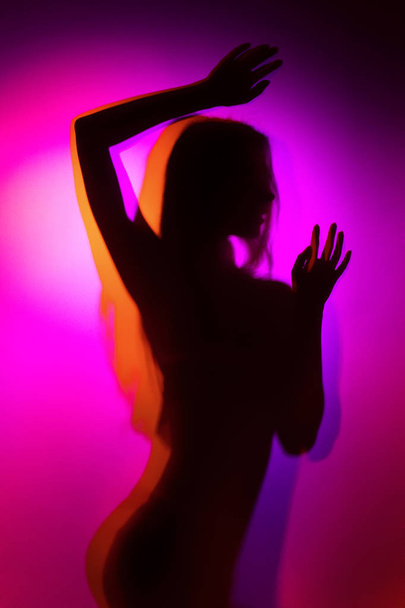 Silhouette of a girl in violet and orange colour light wearing lingerie shot through matte glass - Foto, Imagen