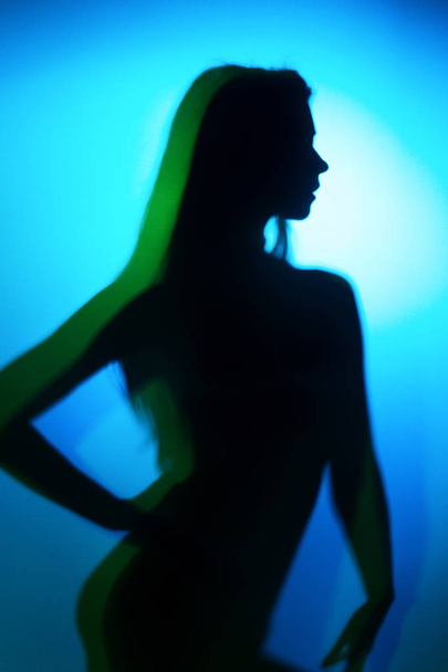 Silhouette of a girl in blue and green colour light wearing lingerie shot through matte glass - Foto, imagen
