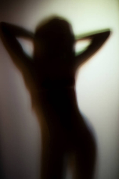 ランジェリーを身に着けている日の光で女の子のシルエットがマットのガラスを通して撮影 - 写真・画像