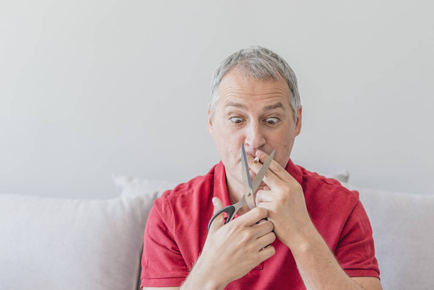 Man trying to quit smoking. Conceptual image. Businessman in red shirt is cutting a cigarette with scissors. Stop smoking concept. Concept of health protection. Quit smoking, health care concept. No smoking. - Foto, immagini