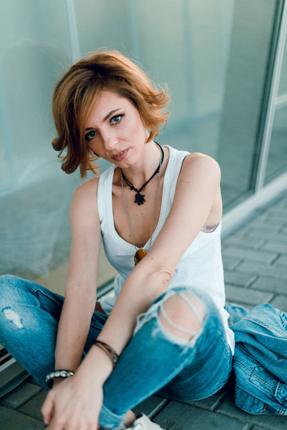 Beautiful fashion woman with  short hair  and make up posing in jeans on city street at sunset - Fotografie, Obrázek