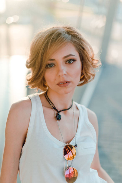 Beautiful fashion woman with  short hair  and make up posing in jeans on city street at sunset - Foto, Imagem