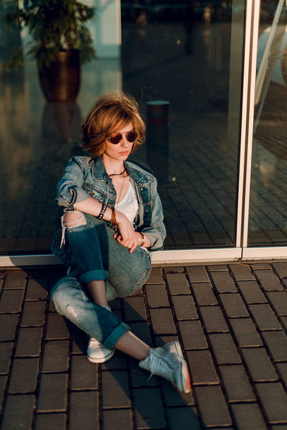 Beautiful fashion woman with  short hair  and make up posing in jeans on city street at sunset - Foto, Bild