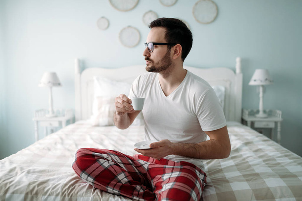 Portrait of handsome young man drinking coffee in bedroom - Foto, Bild