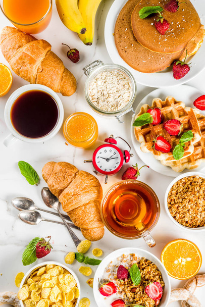 Egészséges reggeli étkezés koncepció, különböző reggel élelmiszer - palacsinta, gofri, croissant zabpehely szendvics és granola, joghurt, gyümölcsök, bogyós gyümölcsök, kávé, tea, narancslé, fehér háttér - Fotó, kép