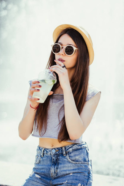 Gülümseyen pozitif komik genç kadın elinde bardak içki, güneş ışığı, açık, street style - Fotoğraf, Görsel
