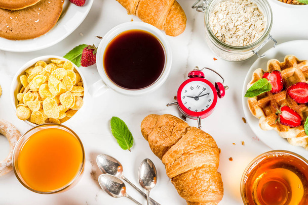 Concepto de desayuno saludable, varios alimentos de la mañana panqueques, gofres, sándwich de avena croissant y granola con yogur, frutas, bayas, café, té, jugo de naranja, fondo blanco
 - Foto, Imagen