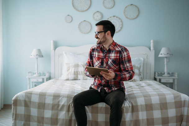 Handsome young man using digital tablet in bedroom - Valokuva, kuva