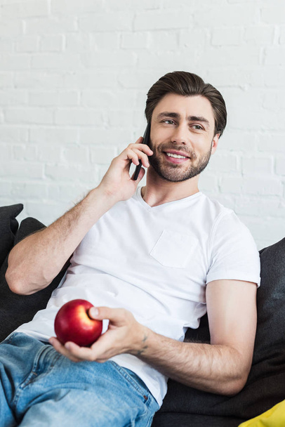 улыбающийся мужчина разговаривает на смартфоне и держит яблоко в руке дома
 - Фото, изображение