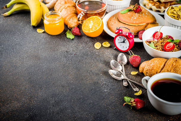 Концепция здорового завтрака, разнообразная утренняя еда - блины, вафли, бутерброды с круассанами и мюсли с йогуртом, фрукты, ягоды, кофе, чай, апельсиновый сок, темно-ржавый фон
 - Фото, изображение