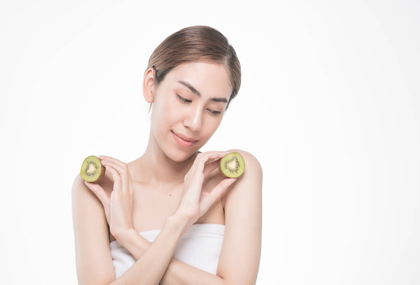beautiful asia woman with towel on head with perfect clean skin smiling holding kiwi slices over white background. Beauty cosmetology and spa. - Foto, afbeelding