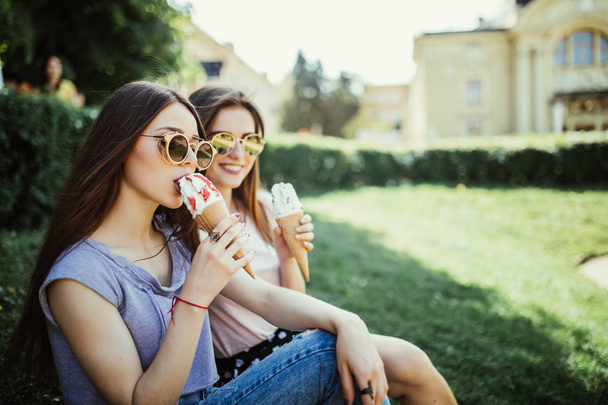 Fiatal két nő meg enni fagylalt ül a fűben, a város utcáin - Fotó, kép