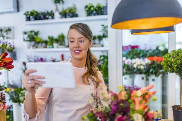 Florist woman taking order online by tablet. Female florist working in flower shop with tablet. Crop shot of salesperson in floral shop using tablet and arranging delivery with app. - Photo, Image