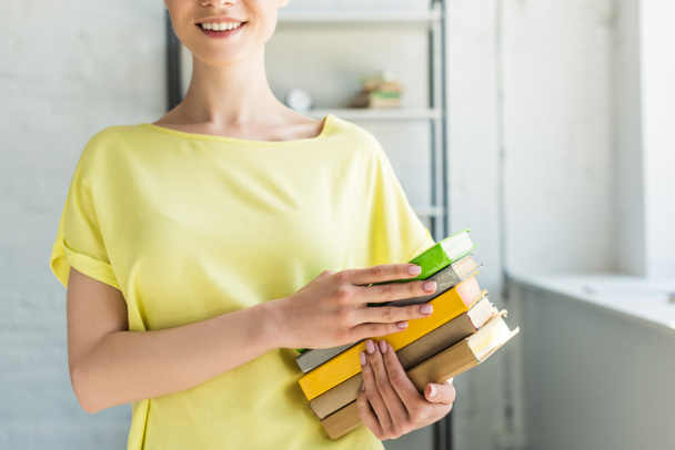 image recadrée d'une jeune femme souriante tenant une pile de livres
 - Photo, image