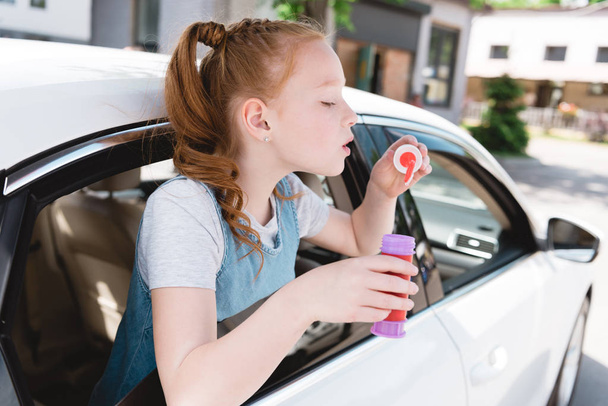 side view of child blowing soap bubbles while sitting in car - Foto, imagen