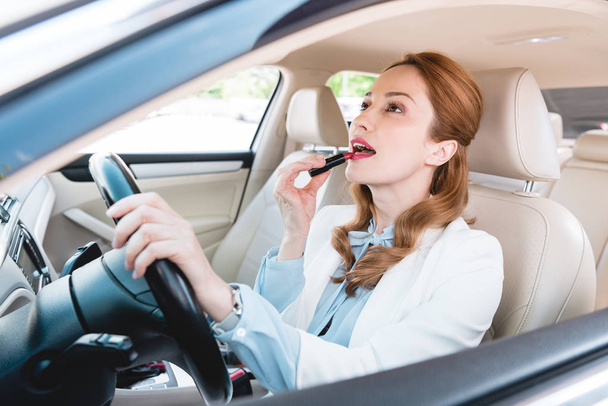vue latérale de la femme d'affaires appliquant rouge à lèvres tout en conduisant voiture
 - Photo, image