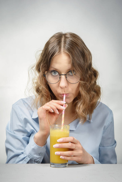 A girl in glasses drinking  orange juice on a gray background - Zdjęcie, obraz