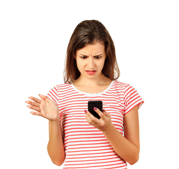 Девочка смущенно смотрит на мобильный телефон или смартфон. эмоциональная девушка изолированы на белом фоне
. - Фото, изображение