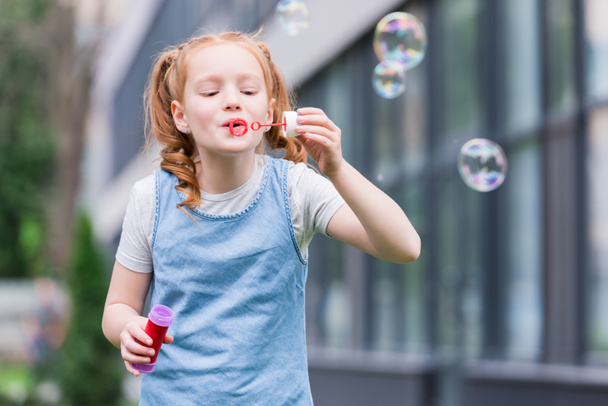 portrait of cute child blowing soap bubbles on street - Fotó, kép