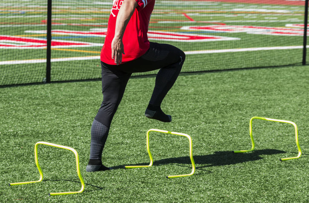 Egy középiskolai atléta steping felső sárga mini gátfutás-nincs cipő, hogy segítse a láb erejét. - Fotó, kép