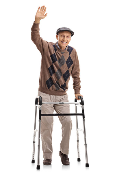 Full length portrait of a senior with a walker waving at the camera isolated on white background - 写真・画像