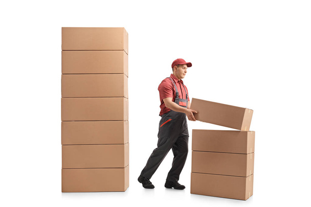 Full length profile shot of a mover placing a package on top of a stack of packages isolated on white background - Fotografie, Obrázek