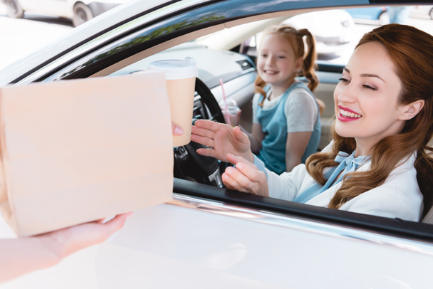 επιλεκτική εστίαση του χαμογελώντας επιχειρηματίας λαμβάνοντας λάβει μακριά την παραγγελία με την κόρη στο κάθισμα επιβατών στο αυτοκίνητο - Φωτογραφία, εικόνα