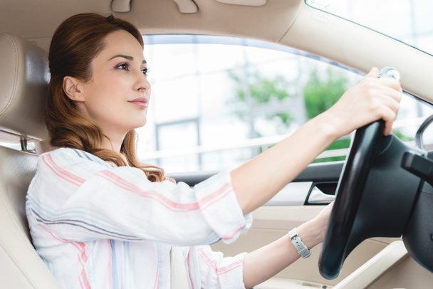 Zijaanzicht van aantrekkelijke vrouw rijdt auto alleen - Foto, afbeelding