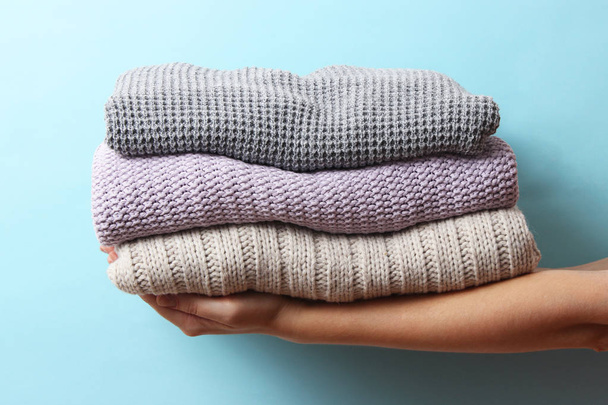 светри, укладені в купу жіночих рук на кольоровому фоні. Мінімалізм
 - Фото, зображення
