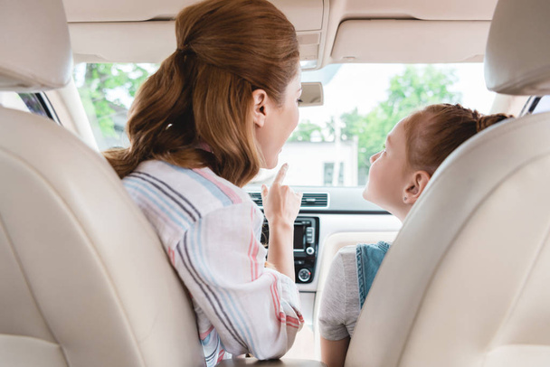 vista trasera de la madre mostrando algo a la hija en el asiento de pasajeros en el coche
 - Foto, Imagen