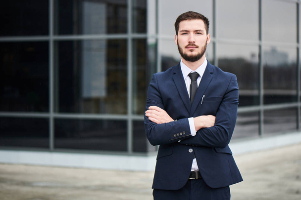 handsome bearded businessman in white shirt and jacket looking at camera while standing with crossed arms near glass building  - Φωτογραφία, εικόνα