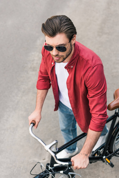 high angle view of stylish young man in sunglasses with bicycle  - Фото, изображение