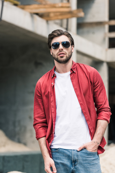 young stylish man in sunglasses at construction building  - Zdjęcie, obraz