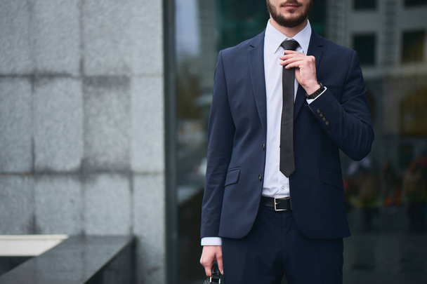 serious bearded businessman in suit straightens tie at street  - Foto, Imagen