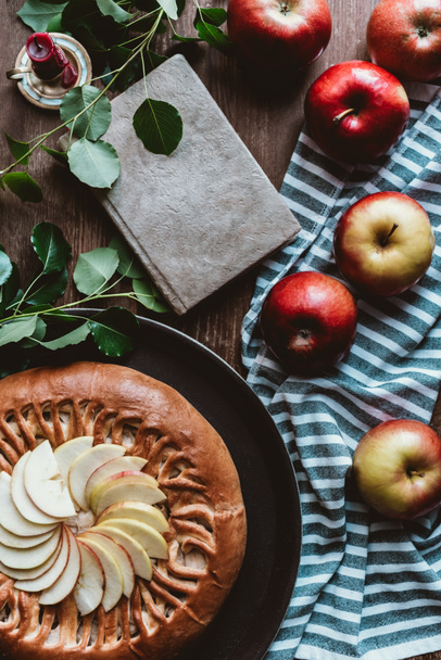 flat lay with arranged homemade apple pie, fresh apples, notebook and linen on wooden tabletop - 写真・画像